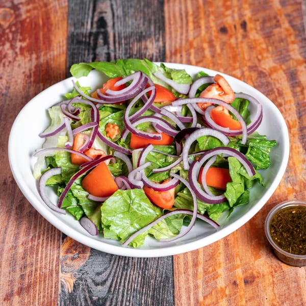 A fresh Kozi Italian Street Food salad with lettuce, tomatoes, red onions, and a side of dressing.