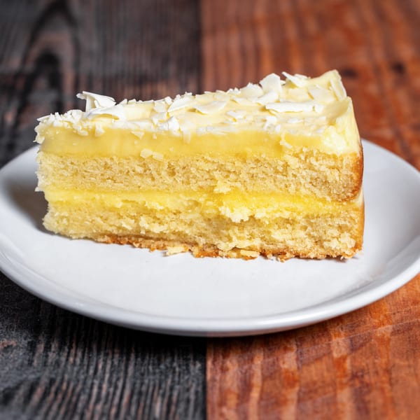 Slice of lemon cake with white chocolate shavings on a white plate at Kozi Italian Street Food.