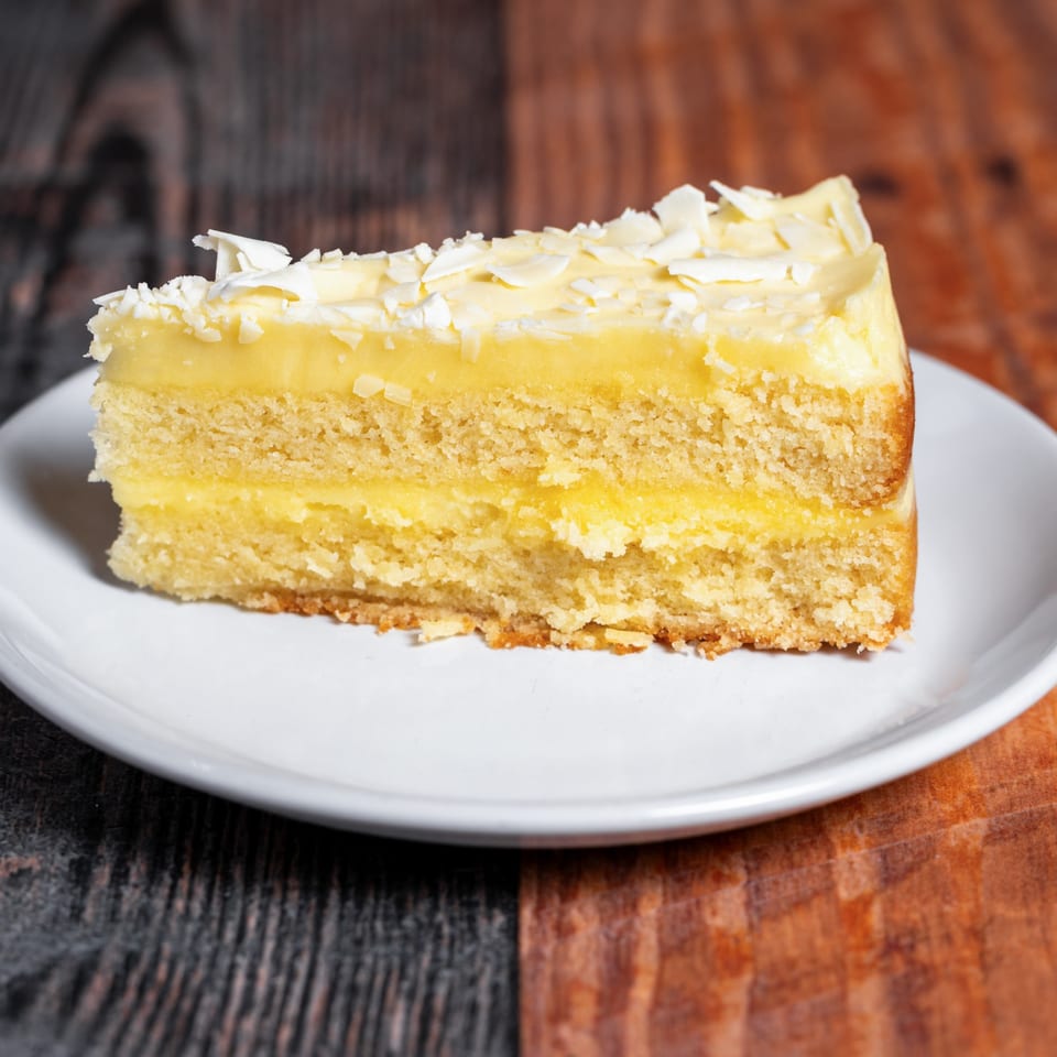 Slice of lemon cake with white chocolate shavings on a white plate at Kozi Italian Street Food.