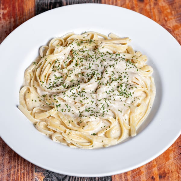 Creamy fettuccine alfredo pasta with parsley on a white plate from Kozi Italian Street Food.