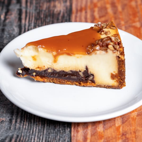 Slice of cheesecake with caramel topping and nuts on a white plate at Kozi Italian Street Food.